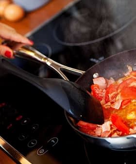 Persona revolviendo una mezcla de tomates picados y tocino en una sartén sobre una estufa. Olive Oil Times