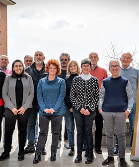Un gruppo di persone in piedi insieme per una foto, con uno striscione sullo sfondo con la scritta "Ercole Olivario". - Olive Oil Times