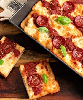 Eine rechteckige Peperonipizza mit Tomatensoße und frischen Basilikumblättern, serviert in einer Backform. - Olive Oil Times