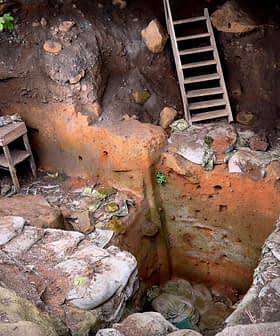 Pozo excavado que muestra una escalera de madera y paredes de piedra con tierra y rocas visibles. - Olive Oil Times