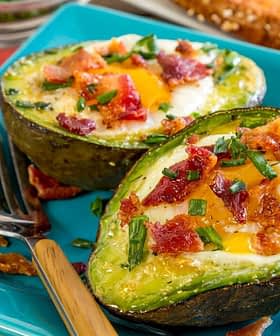 Mitades de aguacate al horno rellenas de huevo, cubiertas con trozos de tocino y cebollino en un plato azul. Olive Oil Times