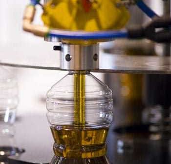 Machine filling a plastic bottle with olive oil during the bottling process. - Olive Oil Times