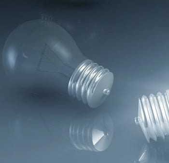 A light bulb with a metallic base and a reflective surface lying on a smooth surface. - Olive Oil Times