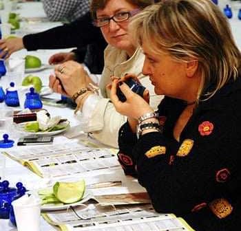 Two women participating in an olive oil tasting event, with green apples and blue tasting cups on the table. - Olive Oil Times
