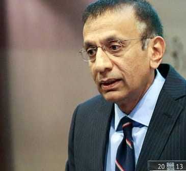 A man in a dark suit and glasses speaking during a presentation at an event. - Olive Oil Times