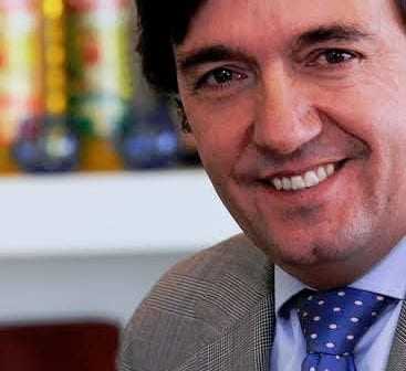 A man wearing a suit and a polka dot tie smiling at the camera. - Olive Oil Times