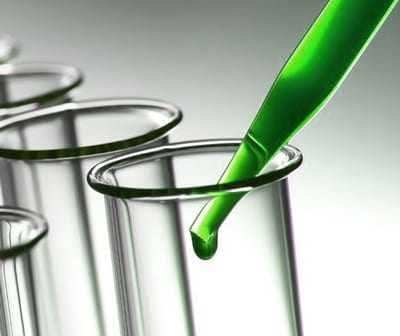 緑色の液体をピペットでガラス試験管に滴下しています。 - Olive Oil Times