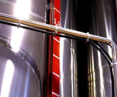Close-up of a stainless steel storage tank with a measurement scale and piping. - Olive Oil Times