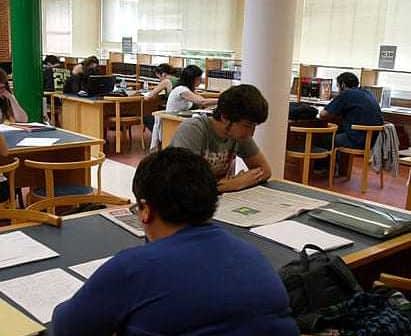 Students engaged in reading and studying at tables in a library setting. - Olive Oil Times