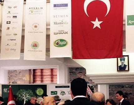 Turkish flag with a white star and crescent displayed at an indoor event with attendees. - Olive Oil Times