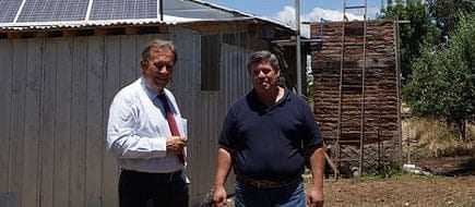 Two men standing outside a building with solar panels on the roof and a wooden structure in the background. - Olive Oil Times