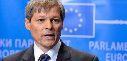 Dacian Ciolos speaking during a press conference in front of a blue backdrop with the European Union flag. - Olive Oil Times