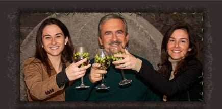 Three individuals, two women and one man, raising glasses filled with grapes in a celebratory manner. - Olive Oil Times