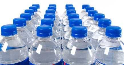 Multiple plastic bottles of water with blue caps arranged in rows. - Olive Oil Times