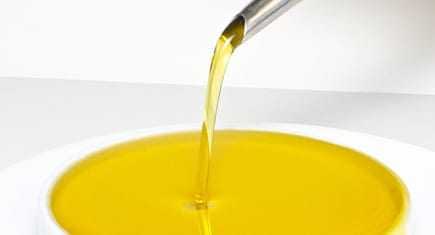 Stream of olive oil being poured from a spout into a white bowl. - Olive Oil Times