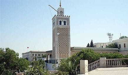 Clock tower with intricate design and a spire located in Tunisia, surrounded by greenery. - Olive Oil Times