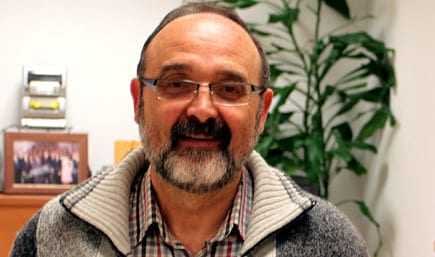 A man with glasses and a beard wearing a gray sweater, smiling in an indoor setting. - Olive Oil Times