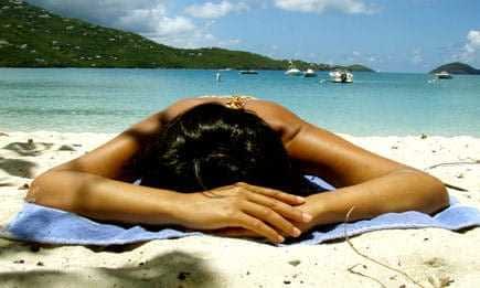 Individual lying face down on a beach towel on a sandy beach near the water. - Olive Oil Times