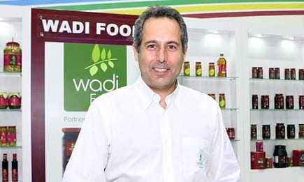 Moški v beli srajci stoji pred blagovno znamko Wadi Food in razstavo izdelkov. - Olive Oil Times