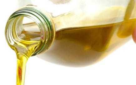A glass bottle pouring olive oil with a clear stream of liquid flowing from the spout. - Olive Oil Times