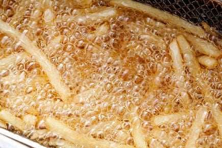 Fried potato strips bubbling in hot oil during the cooking process. - Olive Oil Times