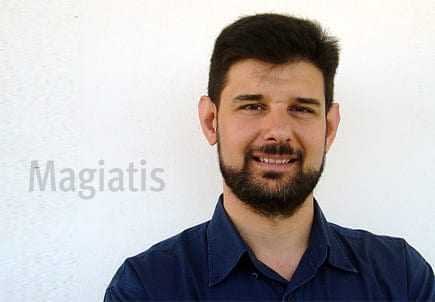 Man with a beard wearing a blue shirt, smiling against a plain background with the name 'Magiatis' next to him. - Olive Oil Times