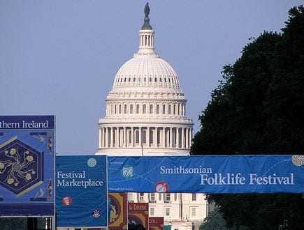 United States Capitol building partially visible behind festival banners at the Smithsonian Folklife Festival. - Olive Oil Times