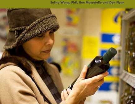 Woman examining a bottle of olive oil while holding a survey document titled 'Consumer Attitudes on Olive Oil'. - Olive Oil Times