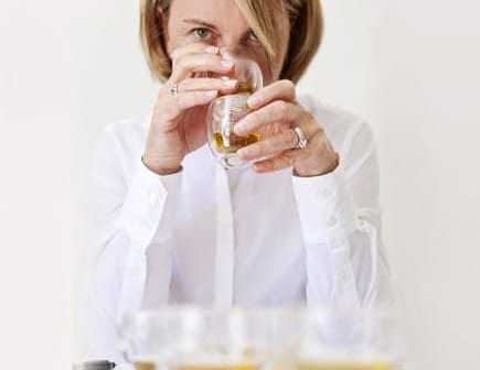 Woman holding a glass of olive oil while tasting it, with several glasses in front of her. - Olive Oil Times