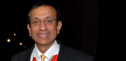 A man wearing a black suit and a tie, smiling at the camera in a formal setting. - Olive Oil Times