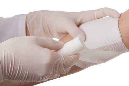 A medical professional in gloves applying a bandage to a patient's arm. - Olive Oil Times