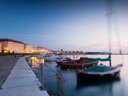 Several boats docked at a harbor with calm water during twilight hours. - Olive Oil Times