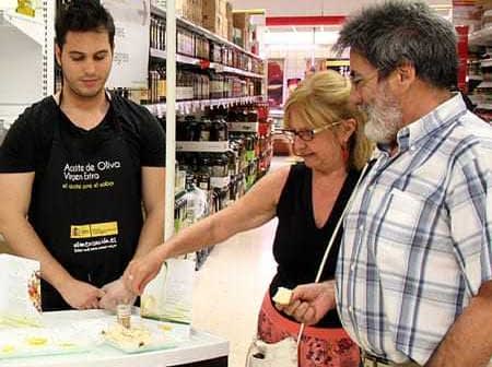 A young man serving olive oil samples to two customers in a store aisle. - Olive Oil Times