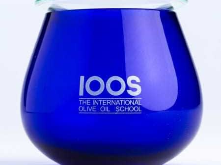 Blue glass container with the logo of The International Olive Oil School printed on it. - Olive Oil Times