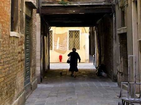 Individual walking through a narrow alleyway with brick walls and a cat following. - Olive Oil Times