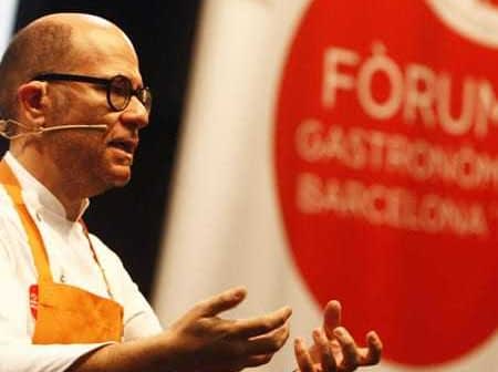 A chef gesturing while speaking at the Gastronomy Forum in Barcelona, wearing an orange apron. - Olive Oil Times