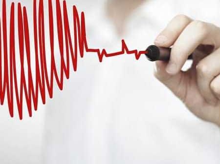 Person's hand drawing a red heartbeat line with a marker on a white background. - Olive Oil Times