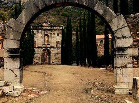 Archway with a stone structure visible in the background, surrounded by tall trees. - Olive Oil Times