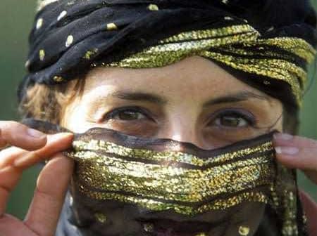 Woman with a decorative black and gold headscarf partially covering her face, revealing her eyes. - Olive Oil Times