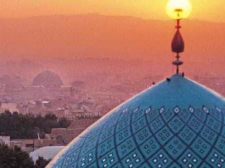 A blue dome with intricate patterns and a sun setting in the background over a city skyline. - Olive Oil Times