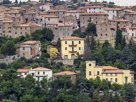 A scenic view of a Tuscan village with stone buildings and terracotta roofs surrounded by greenery. - Olive Oil Times