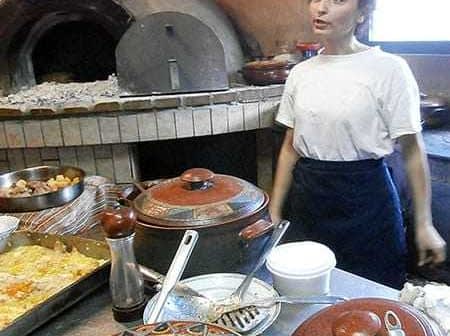 Woman standing in a kitchen with various cooking pots and an oven in the background. - Olive Oil Times