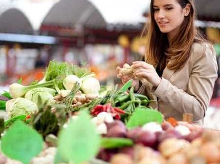 A woman examining fresh vegetables at a market stall filled with various produce. - Olive Oil Times