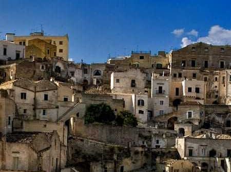 A view of historic stone buildings stacked on a hillside in Matera, Italy under a blue sky. - Olive Oil Times