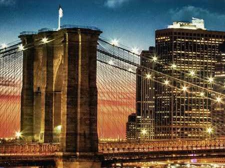 Brooklyn Bridge with illuminated towers and city skyline during sunset. - Olive Oil Times