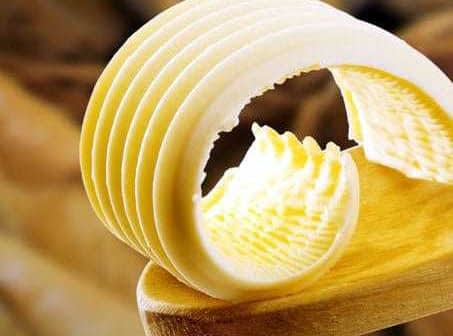 Slices of butter arranged on a wooden spoon with a smooth texture. - Olive Oil Times