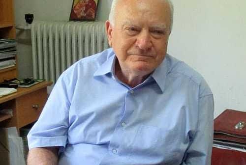 Elderly man with gray hair wearing a blue shirt seated at a desk with a radiator in the background. - Olive Oil Times