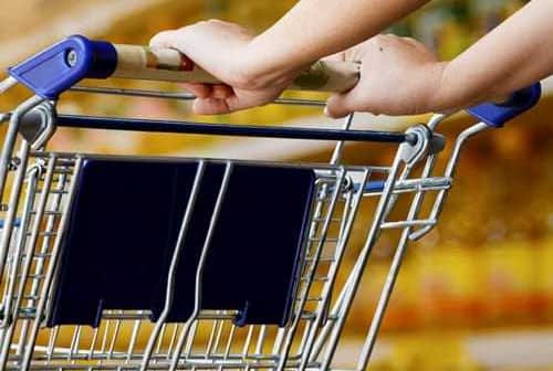 Close-up of a person's hand holding the handle of a shopping cart in a store. - Olive Oil Times