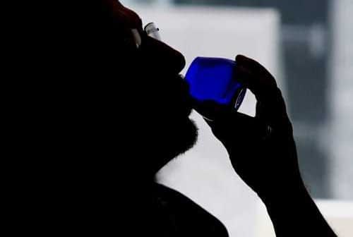 Silhouette of a person holding a blue glass to their lips while drinking. - Olive Oil Times