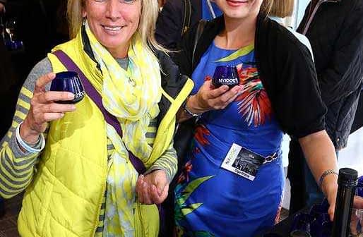 Two women holding glasses at a social event, one wearing a yellow vest and the other in a floral dress. - Olive Oil Times